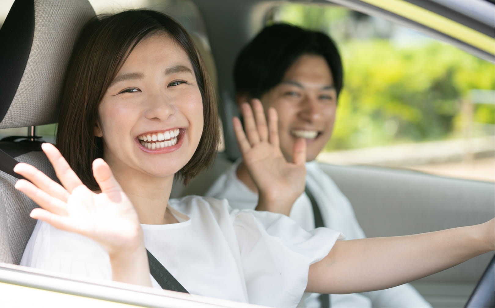 手を挙げている運転中の女性と助手席の男性